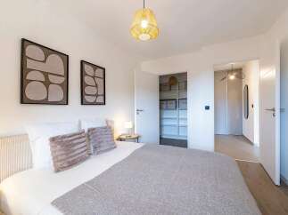 Experience modern comfort in this beautifully appointed bedroom, featuring a plush bed adorned with decorative pillows and a cozy grey throw.