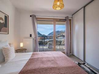 Experience breathtaking mountain views from this charming bedroom, featuring a plush bed adorned with a soft pink throw and fluffy pillows.