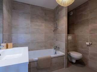 Experience modern comfort in this beautifully tiled bathroom, featuring a sleek white bathtub and a convenient wall-mounted toilet.
