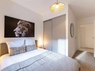 This modern bedroom features a striking black and white lion portrait above a comfortable bed adorned with plush pillows and a soft grey blanket.