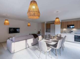 Experience modern living in this open-concept space featuring a stylish dining area with a large table and comfortable seating, adjacent to a sleek, fully-equipped kitchen with ample cabinet space and modern appliances.