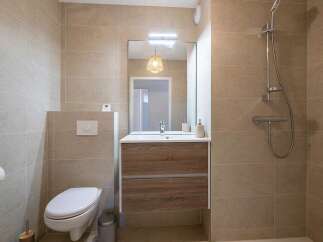 This modern bathroom features a sleek vanity with a wooden finish, complemented by a large mirror and a stylish pendant light.