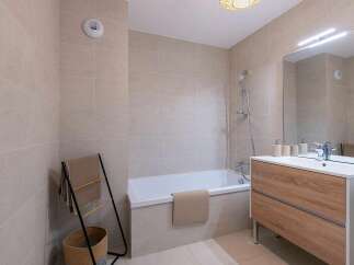 Experience modern comfort in this beautifully tiled bathroom, featuring a sleek bathtub and a stylish wooden vanity with a spacious countertop.