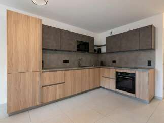 Discover this modern kitchen featuring sleek, light wood cabinetry complemented by sophisticated dark grey countertops and backsplash.
