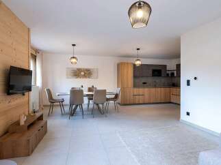 This modern open-plan living space features a sleek kitchen with wood cabinetry and integrated appliances, seamlessly flowing into a dining area with a stylish table and chairs.