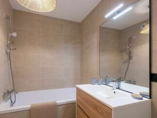 This modern bathroom features a sleek white bathtub with a chrome showerhead and faucet, complemented by large, neutral-toned tiles on the walls.