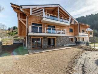 Experience modern alpine living in this stunning wooden house, featuring a striking stone base and multiple balconies offering picturesque views.