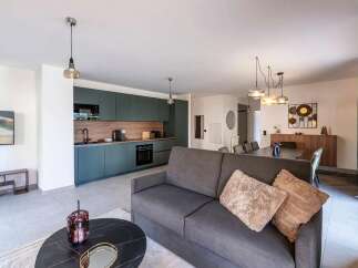 This modern open-plan living space features a sleek, dark teal kitchen with integrated appliances and ample cabinet storage.