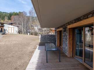Experience modern mountain living with this stunning property featuring a spacious wooden deck and a sleek glass-top dining table, perfect for al fresco meals.