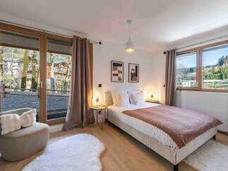 Experience serene mountain living in this beautifully appointed bedroom, featuring a comfortable bed, elegant decor, and large windows that flood the space with natural light.