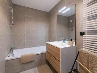 This modern bathroom features a sleek bathtub with a showerhead, complemented by large, neutral-toned tiles on the walls.
