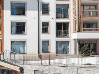 Experience luxury mountain living in this stunning modern building, featuring a unique wooden facade and expansive windows that offer breathtaking views.
