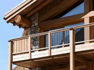 Experience luxury mountain living with this stunning chalet featuring a spacious balcony and intricate log and stone architecture.
