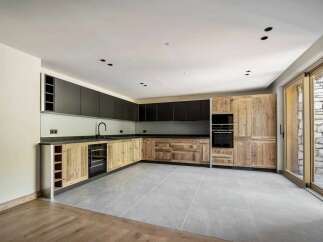 Discover this modern kitchen featuring sleek dark upper cabinets contrasted with rustic wooden lower cabinets and a wine rack.