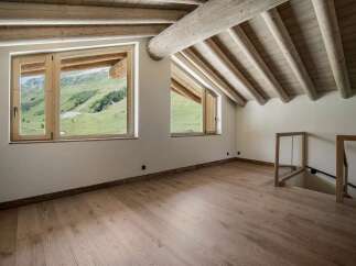 Experience breathtaking mountain views from this charming attic room, featuring a vaulted ceiling with exposed wooden beams and large windows that flood the space with natural light.