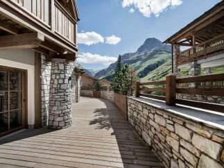 Experience luxury mountain living in this stunning property featuring a charming wooden walkway leading to a stone-clad building.