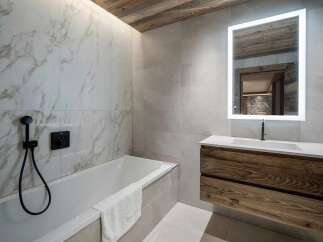 Experience luxury in this modern bathroom featuring a sleek bathtub with a marble-tiled accent wall and a black shower fixture.