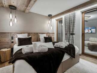 Experience luxury mountain living in this beautifully appointed bedroom, featuring two comfortable beds adorned with plush dark brown throws and crisp white linens.