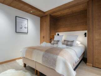 Experience cozy mountain living in this beautifully appointed bedroom, featuring a plush bed adorned with a warm, checkered throw and soft white towels.