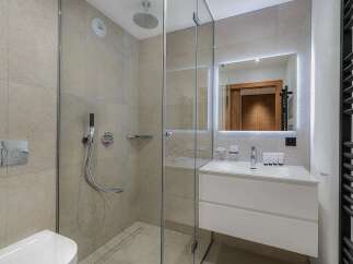 Experience modern luxury in this stunning bathroom featuring a spacious walk-in shower with a rainfall showerhead and a sleek vanity with a backlit mirror.