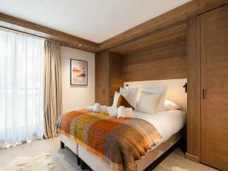 Experience cozy mountain living in this charming bedroom, featuring a plush bed adorned with a vibrant, checkered throw blanket and crisp white towels.