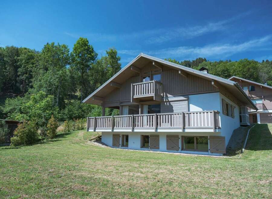 Experience the charm of this alpine chalet, nestled amidst lush greenery and under a clear blue sky.