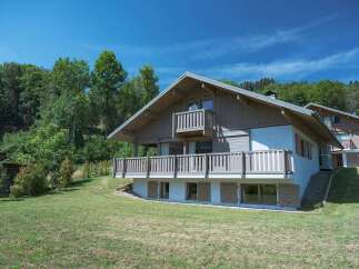 Experience the charm of this alpine chalet, nestled amidst lush greenery and under a clear blue sky.