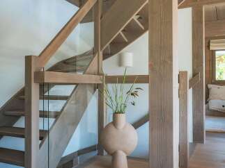 Experience modern living with this stunning staircase featuring natural wood beams and sleek glass railings.
