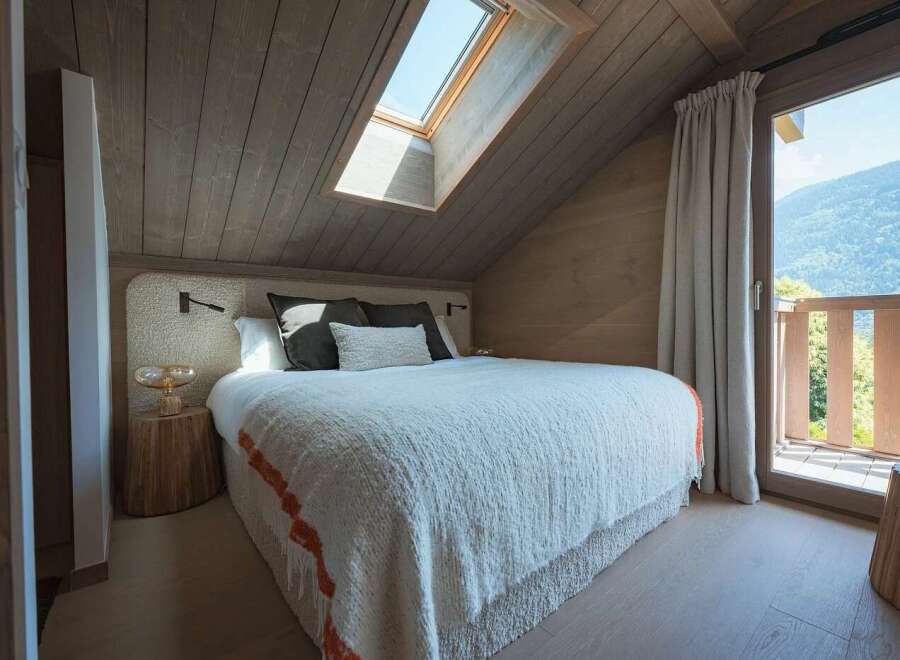 Experience cozy mountain living in this charming bedroom featuring a plush bed adorned with a textured white duvet and subtle orange trim.