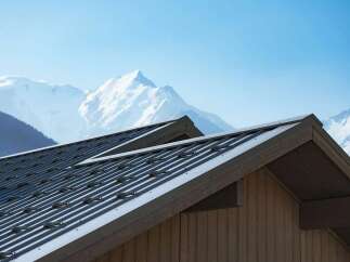 Experience luxury mountain living with this stunning property featuring a modern metal roof and rustic wooden siding, perfectly complementing the majestic snow-capped peaks in the background.