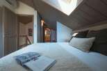Experience cozy living in this charming attic bedroom, featuring a plush bed adorned with soft linens and decorative pillows.