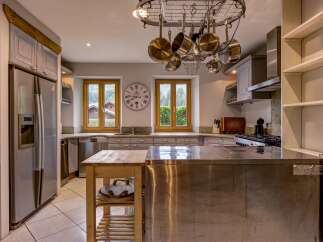 Experience rustic charm and modern convenience in this spacious kitchen, featuring a large stainless steel island and a pot rack overhead.