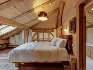 Experience rustic charm in this cozy attic bedroom, featuring exposed wooden beams and a sloping ceiling with skylights that flood the space with natural light.