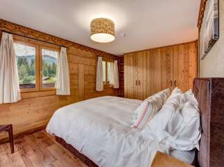 Experience rustic charm in this cozy mountain bedroom, featuring warm wood paneling and a large window with breathtaking views of the surrounding forest and peaks.
