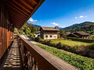 Experience the charm of this alpine retreat, featuring a rustic wooden balcony offering picturesque views of the surrounding mountains and lush greenery.