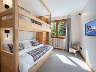 This charming bedroom features a cozy wooden bunk bed with plaid bedding and decorative pillows, perfect for a family or guests.