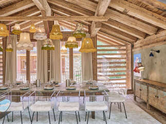 Experience rustic charm and modern elegance in this stunning dining room, featuring a grand wooden table set for a feast and illuminated by a whimsical collection of vintage-inspired lampshades.