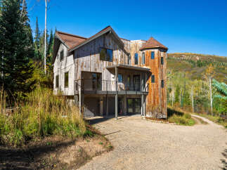 Nestled amidst a vibrant autumn landscape, this unique mountain home boasts a striking architectural design with rustic wood siding and a distinctive turret.