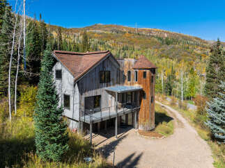 Nestled amidst a vibrant autumn landscape, this unique home features a striking rustic wood exterior and a distinctive turret.