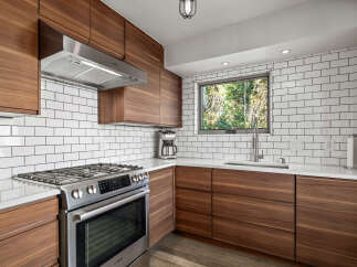This modern kitchen boasts sleek walnut cabinetry and a striking white subway tile backsplash, creating a warm yet contemporary aesthetic.