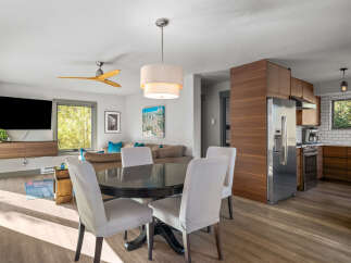 This open-concept living space features a modern dining area with a dark wood table and upholstered chairs, seamlessly flowing into a comfortable living room with a large sectional sofa and a wall-mounted TV.