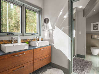 Experience modern luxury in this stunning bathroom featuring a double vanity with vessel sinks and sleek wooden cabinetry.