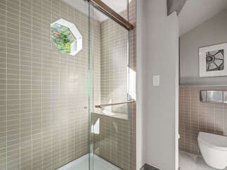 Experience modern luxury in this stunning bathroom featuring a sleek glass-enclosed shower with a unique octagonal window offering natural light.