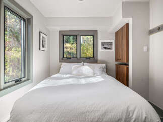 Experience serene living in this cozy bedroom, featuring a comfortable queen-size bed bathed in natural light from large windows.