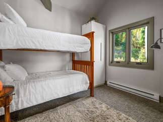 This cozy bedroom features a space-saving wooden bunk bed with crisp white linens, perfect for accommodating guests or children.