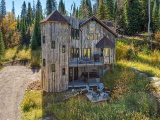 Nestled amidst a vibrant autumn forest, this unique home boasts a striking rustic wood exterior and a distinctive turret.