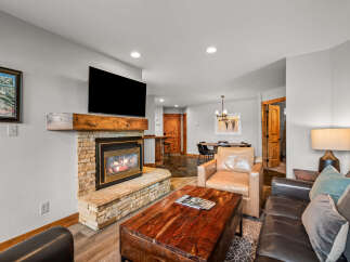 Cozy up by the stone fireplace in this inviting living room, featuring a large flat-screen TV and a rustic wooden mantel.