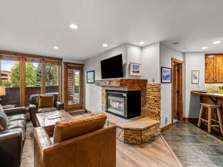 Cozy living room featuring plush leather seating arranged around a rustic stone fireplace with a modern television mounted above.