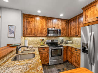 This kitchen boasts beautiful custom wooden cabinetry, complemented by granite countertops and a stone tile backsplash.