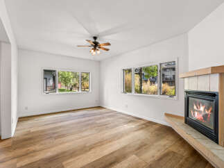 Cozy up by the fireplace in this inviting living space, featuring warm wood-look flooring and a ceiling fan for year-round comfort.